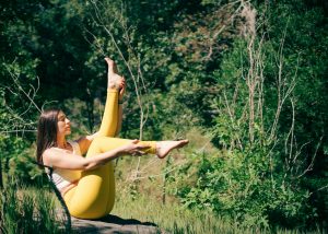 Une femme en leggings jaunes pratique le yoga en plein air entourée de verdure luxuriante.