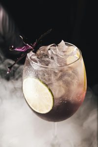 Cocktail rafraîchi dans un verre avec une tranche de citron vert et une garniture vibrante sur un fond enfumé.