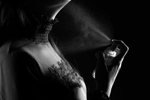 Une femme stylée vaporise du parfum, capturée dans une prise de vue dramatique en noir et blanc en studio.