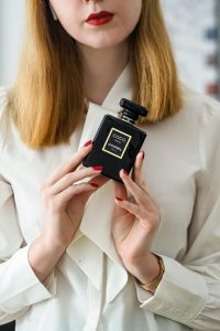 Stylish woman in white blouse holding luxury perfume indoors. Femme élégante en chemisier blanc tenant un parfum de luxe à l'intérieur.