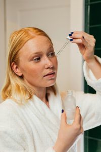 Woman en robe appliquant un sérum de soin sur son visage avec une pipette dans le cadre d'une routine de soin personnelle.