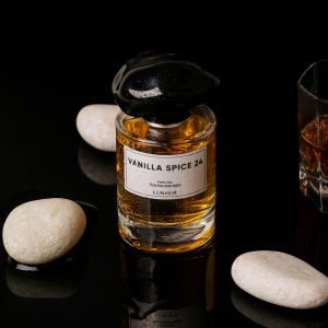 Un flacon de parfum luxueux avec un bouchon noir, posé sur un fond noir avec des pierres.