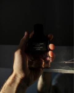 Une main d'homme tient un flacon de parfum Givenchy avec un éclairage dramatique.