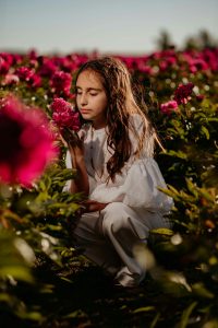 Une jeune fille profitant de la beauté sereine et du parfum des pivoines en fleurs dans un champ vibrant.
