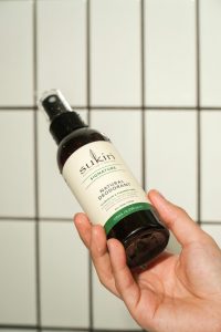Main tenant un déodorant naturel Sukin avec un mur carrelé en arrière-plan, mettant en avant les soins personnels écologiques.