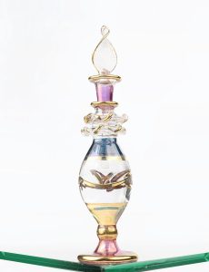 Ornate glass perfume bottle with gold accents on a clear surface. Ideal for lifestyle and fashion themes. Flacon de parfum en verre orné avec des accents dorés sur une surface claire. Idéal pour les thèmes de style de vie et de mode.