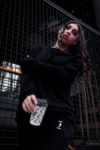Femme confiante en tenue noire tenant un café devant un fond urbain à Téhéran, Iran.