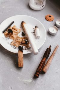 A tranquil still life featuring burning palo santo, candles, and meditation tools on a plate. Une nature morte tranquille mettant en scène du palo santo brûlant, des bougies et des outils de méditation sur une assiette.