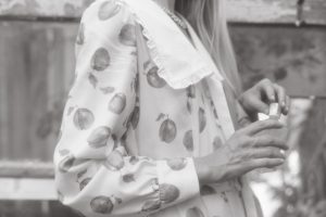Black and white photo of a person in a floral dress holding a bottle. Photo en noir et blanc d'une personne portant une robe à fleurs tenant une bouteille.