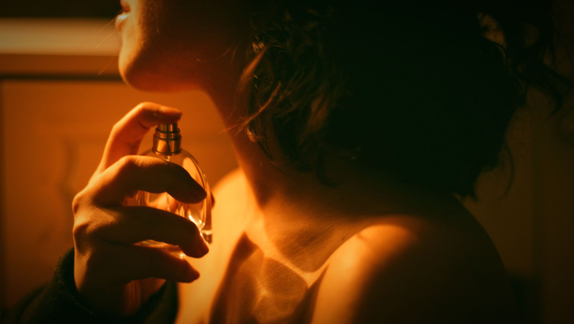 Femme appliquant du parfum sous une lumière chaude