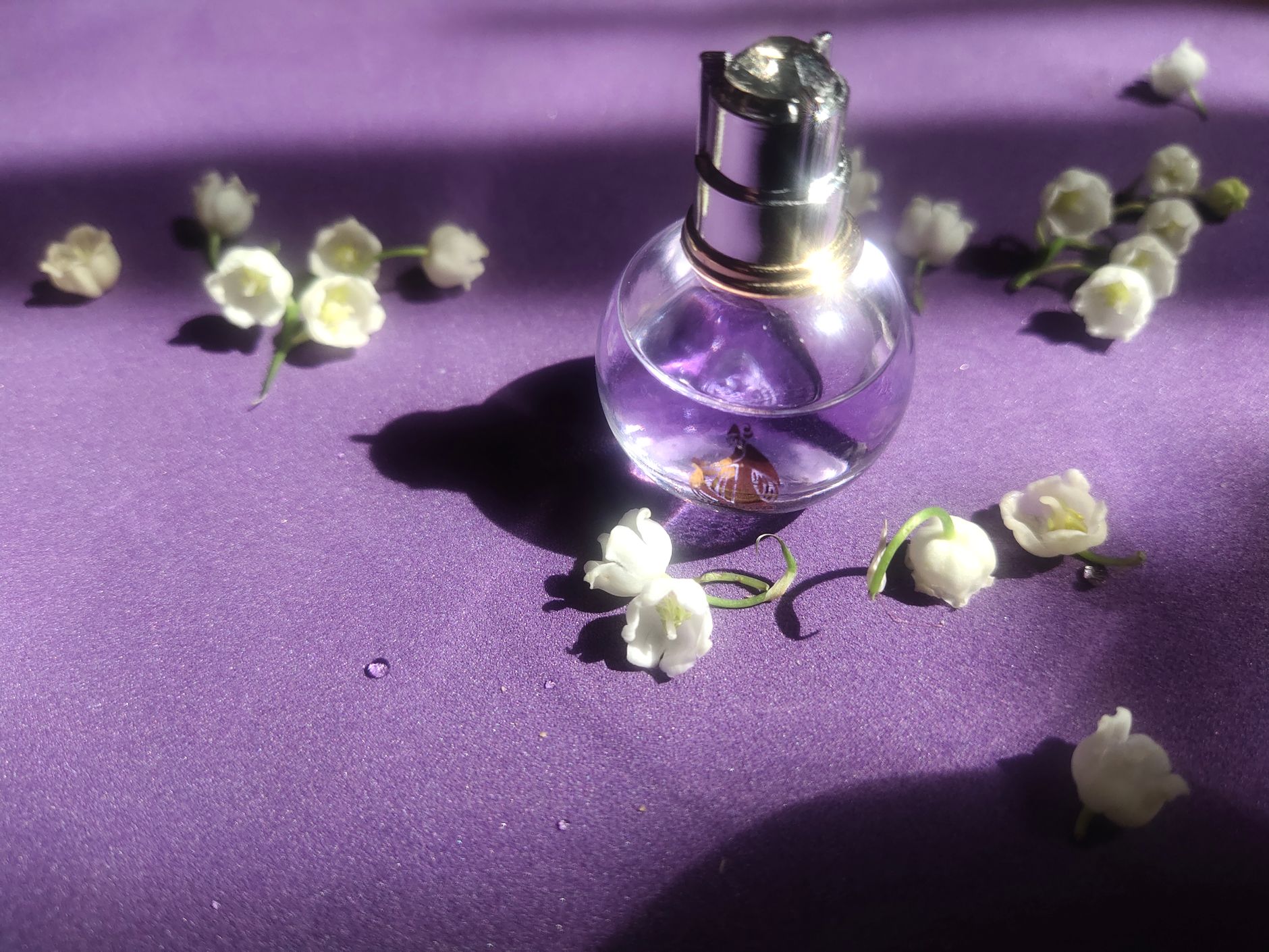 Flacon de parfum parmi des brins de muguet